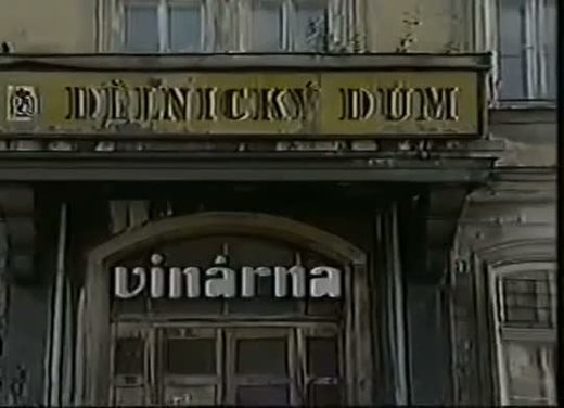 The facade of a town building in Jihlava, the words Delnicky dum, the Workers' House, in gold letters on a long sign above the arched doorway, and a painted wine bar sign under it