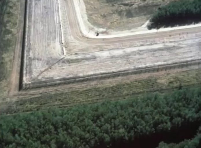 An aerial view of a fence line and a patrol strip turning at almost a right angle through pine forest and fields