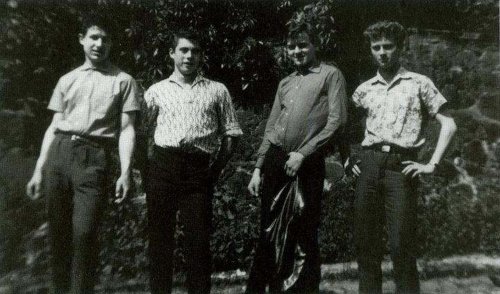 Four teenage boys in summer shirts standing in a row in front of a hedge; Michael is third from the left
