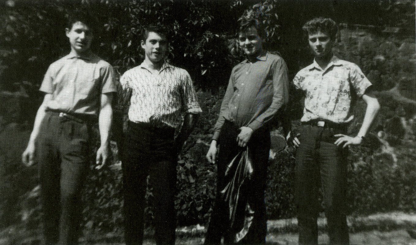 Four teenage boys in summer shirts standing in a row in front of a hedge; Michael is third from the left