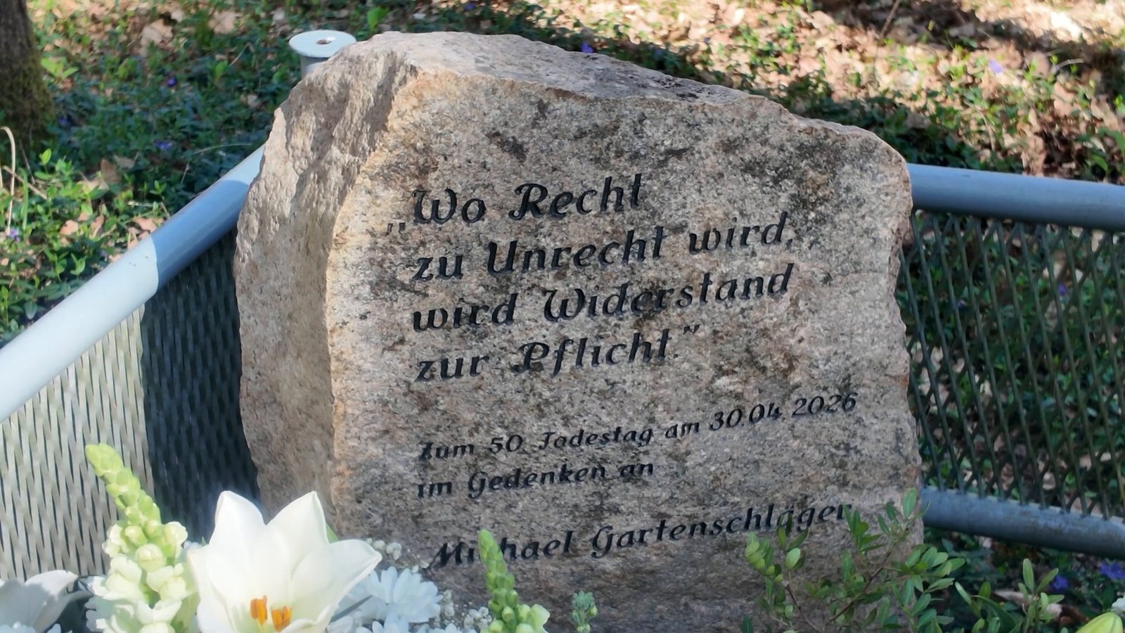 A granite stone engraved Wo Recht zu Unrecht wird, wird Widerstand zur Pflicht, Zum 50. Todestag am 30.04.2026 im Gedenken an Michael Gartenschläger, with white lilies in front