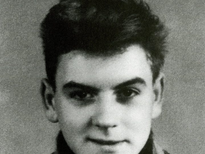 A black and white portrait of Michael Gartenschläger as a teenager, with dark swept-back hair, a scarf and a jacket