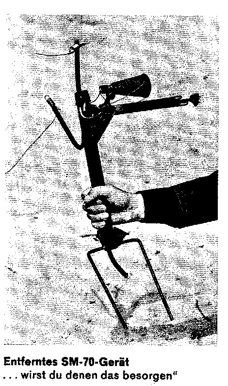 A hand holding up the removed device on its bracket against a pale background; captioned Entferntes SM-70-Gerät