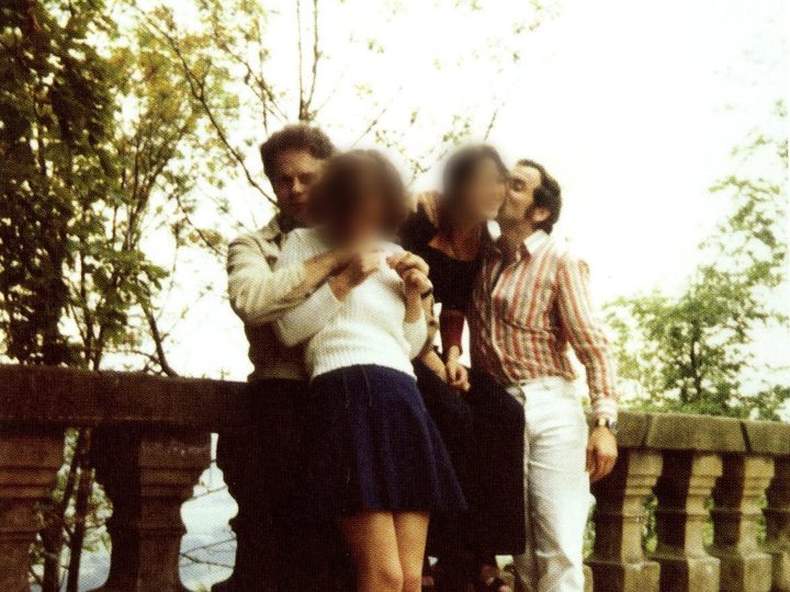 Two young men with two women by a stone balustrade among trees; the women's faces are blurred