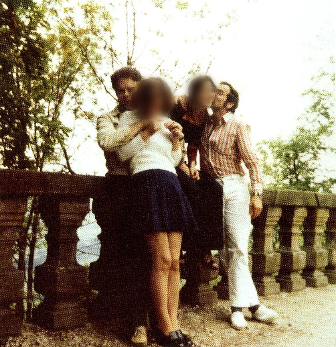 Two young men with two women by a stone balustrade among trees; the women's faces are blurred