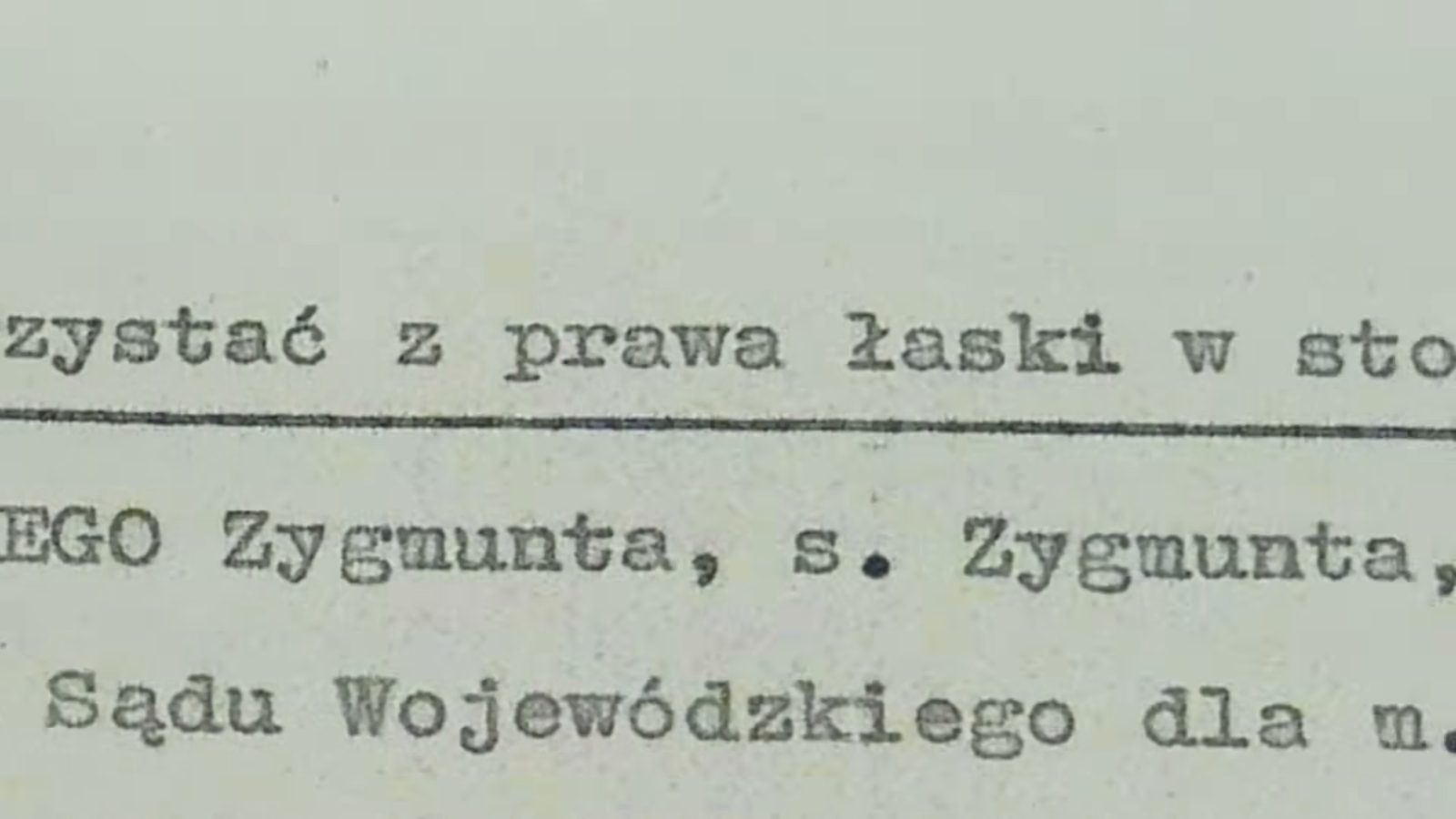 A close-up of typewritten lines on yellowed paper: z prawa łaski, Zygmunta, s. Zygmunta, Sądu Wojewódzkiego dla m.