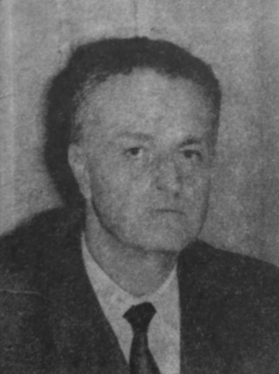 A black and white portrait of a middle-aged man with greying hair, in a dark jacket, a white shirt and a dark tie