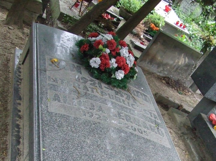 A grey granite grave slab with an engraved inscription and a bunch of red and white flowers at its head