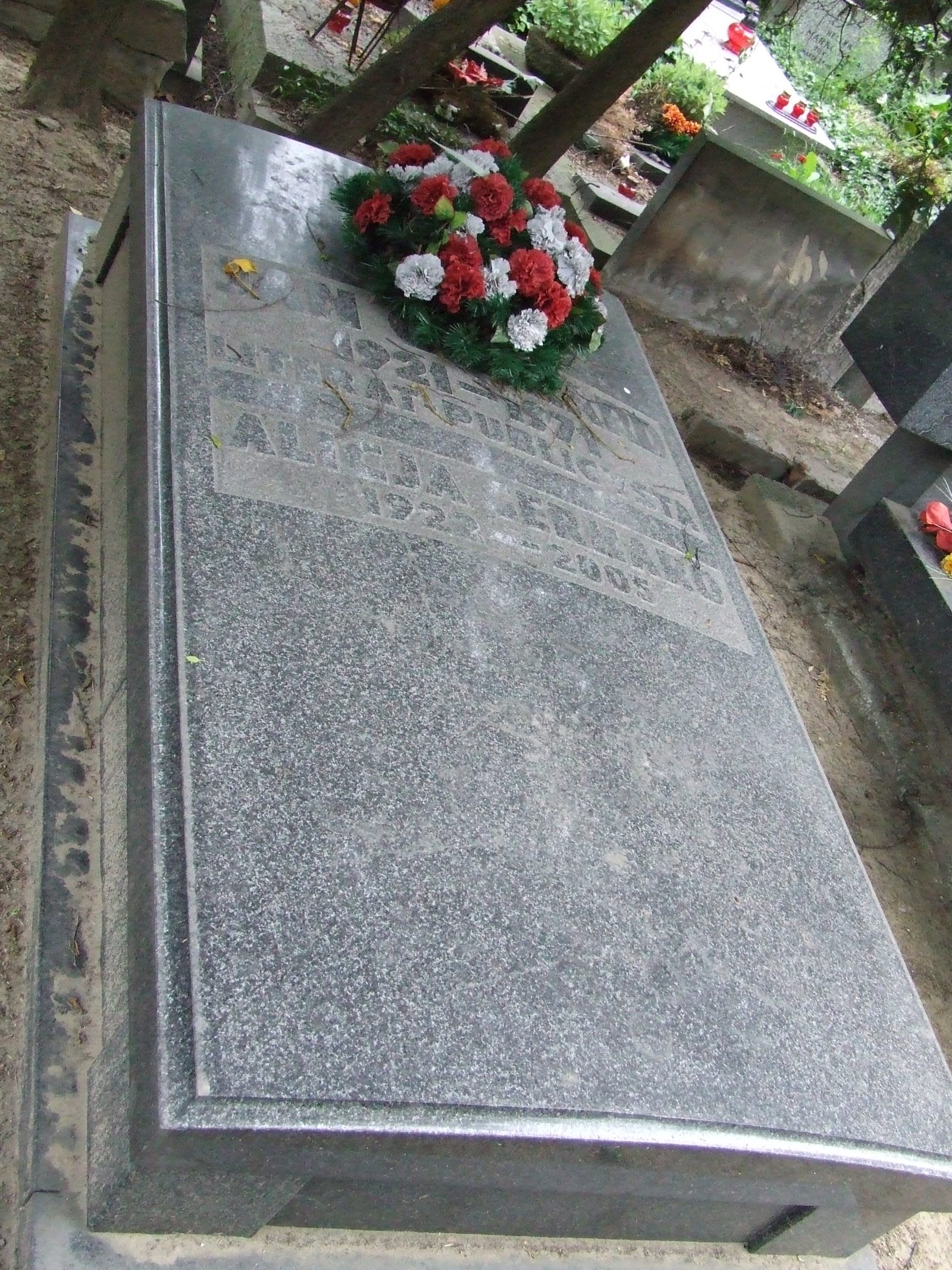 A grey granite grave slab with an engraved inscription and a bunch of red and white flowers at its head