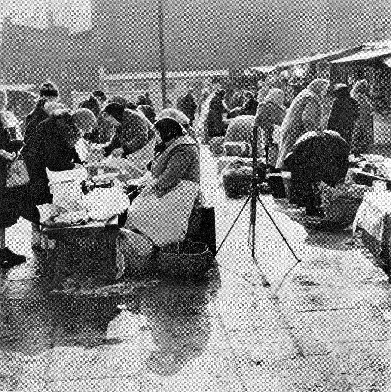 A black and white photograph of women in headscarves selling goods at a crowded outdoor market