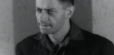 Igor Sevianu, head and shoulders, filmed in black and white against a bare plaster wall