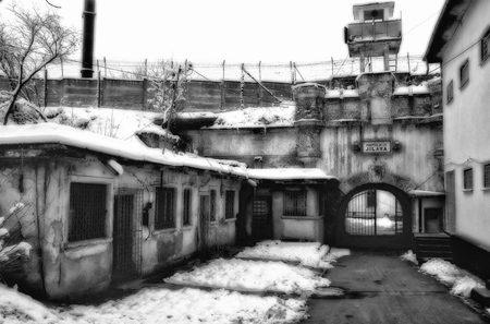 A snow covered yard inside Jilava prison, with a watchtower, barbed wire along the wall and a gate marked Jilava