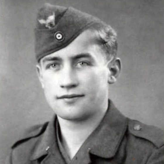 A black and white studio portrait of a young soldier in a German army side cap and tunic, looking slightly to one side