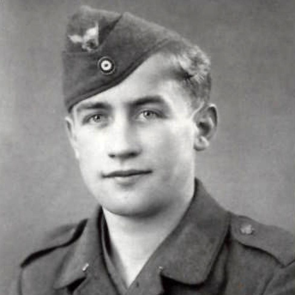 A black and white studio portrait of a young soldier in a German army side cap and tunic, looking slightly to one side