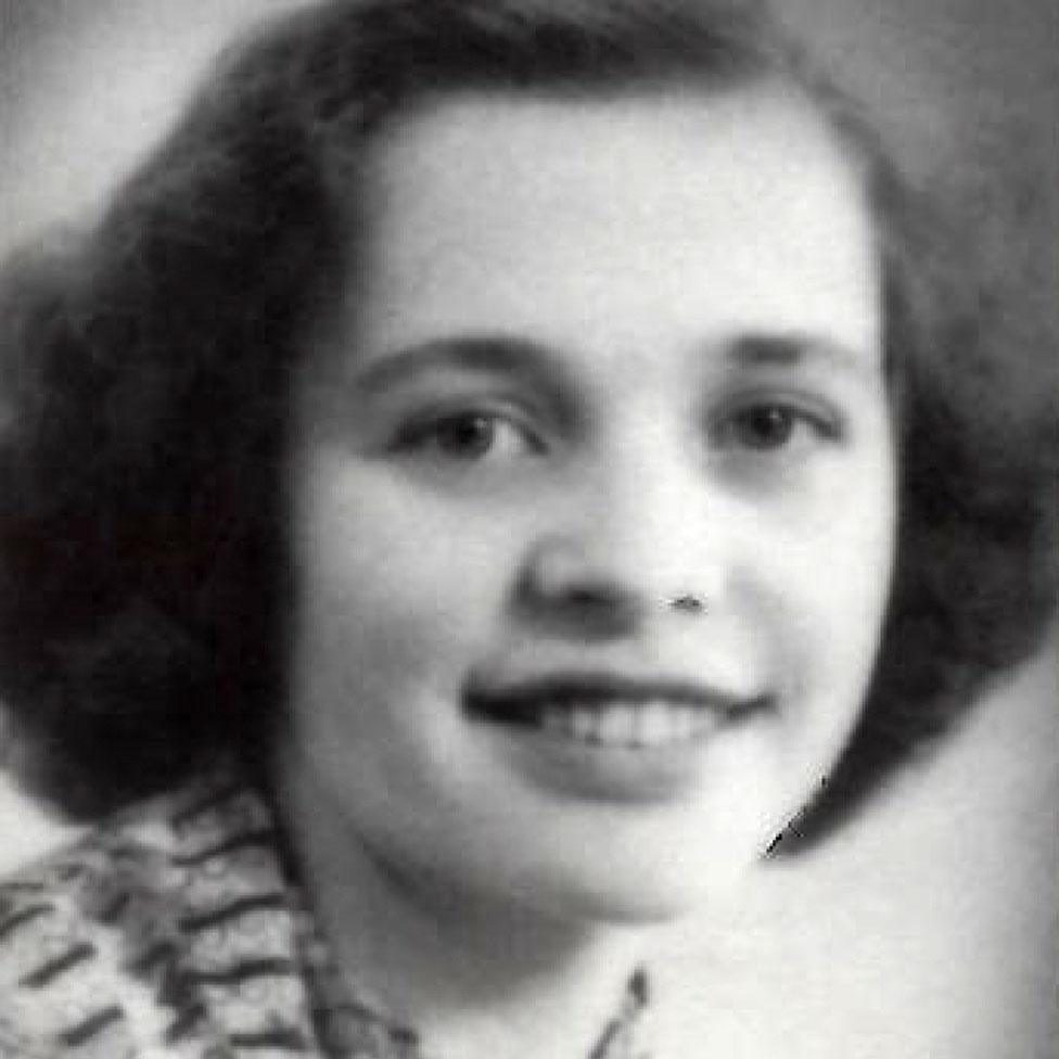 A black and white portrait of a smiling young woman with dark wavy hair, in a patterned knitted cardigan