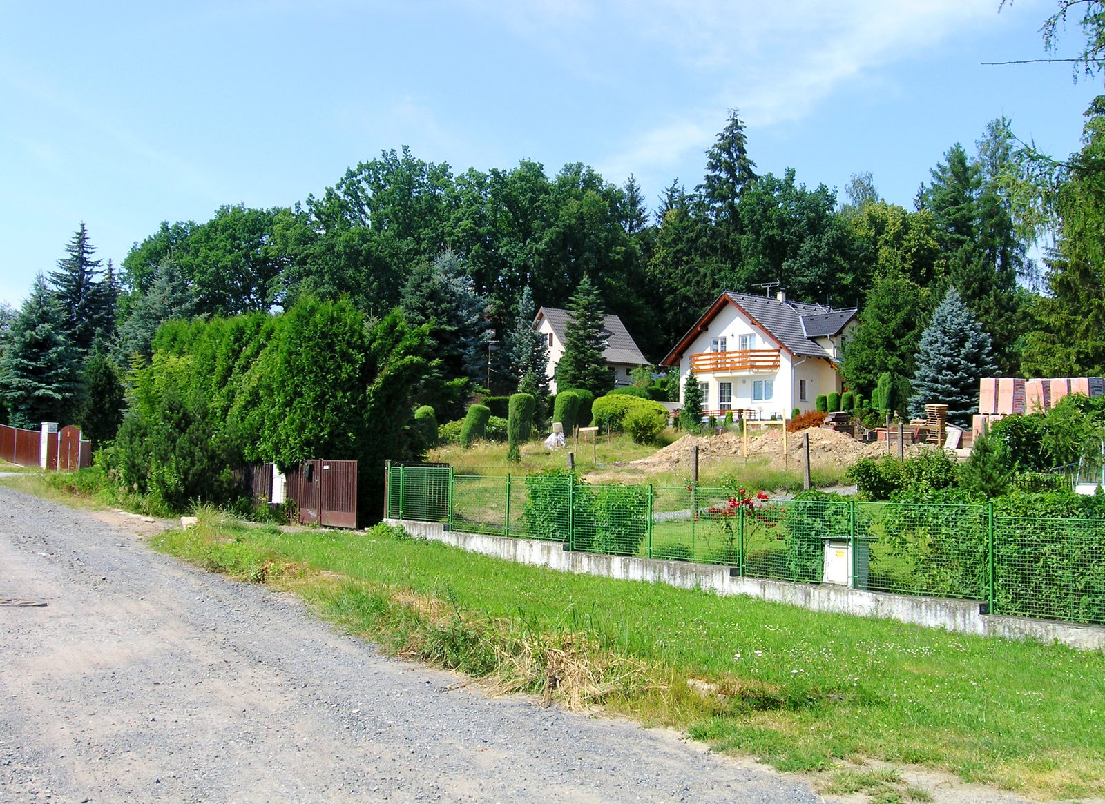 A large pale country house with a steep roof standing among mature trees, seen from a lawn