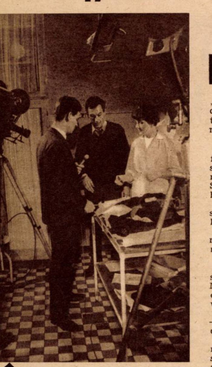 Press photograph of the Kek Feny television crew at work, a camera on a tripod and a microphone held out over a table