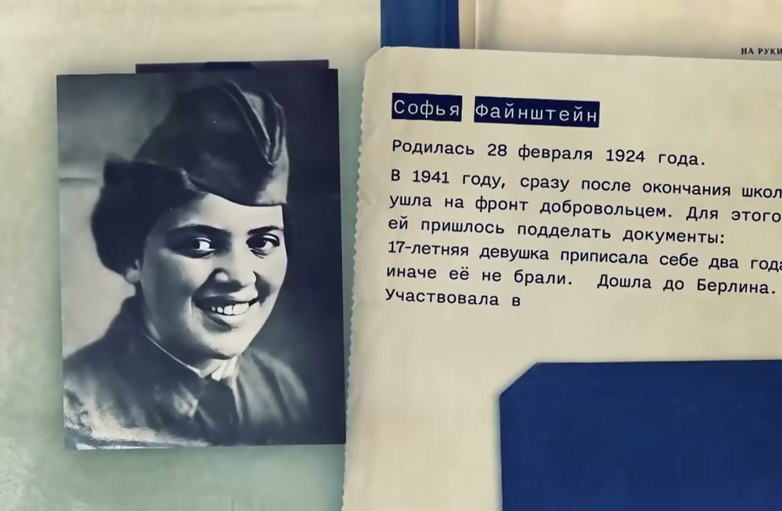 A file page in a documentary: a wartime photograph of a smiling young woman in uniform and forage cap, beside typed Russian lines saying Sofia Fainshtein, born 28 February 1924, left for the front as a volunteer in 1941 after forging her papers to add two years, and reached Berlin