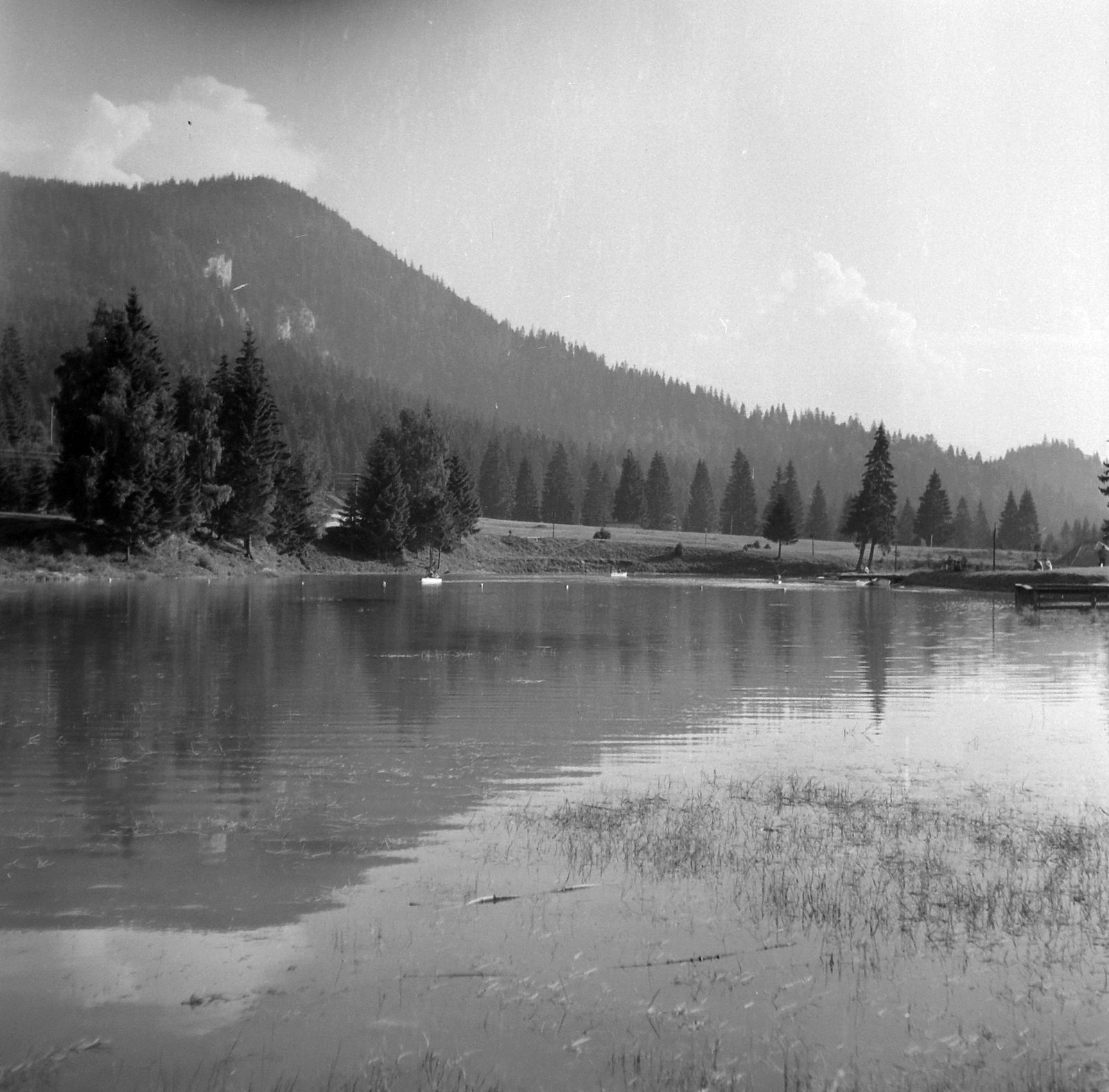 The lake at Poiana Brașov in 1961, small boats on the water, spruce woods along the far shore and the wooded flank of the Postăvarul massif behind