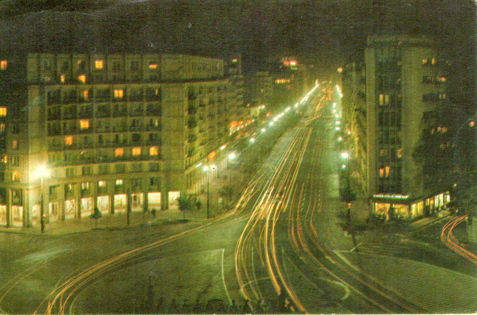 Piața Romană in Bucharest at night in the 1970s, apartment blocks lit from inside and the boulevard streaked with the light trails of traffic