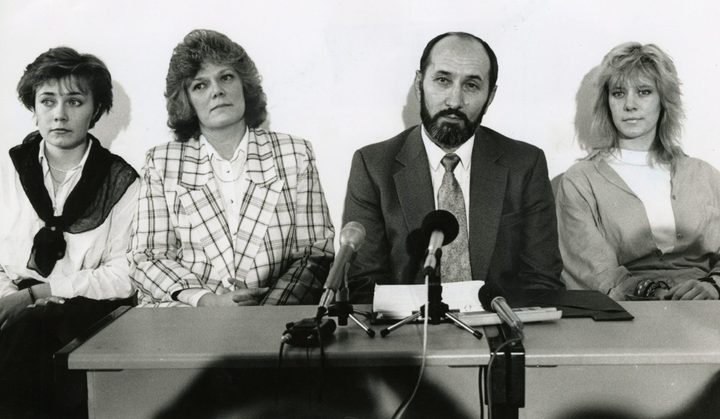 A black and white photograph of Nikola Stedul at a table of microphones with his wife Shirley beside him and their two daughters at either end of the table
