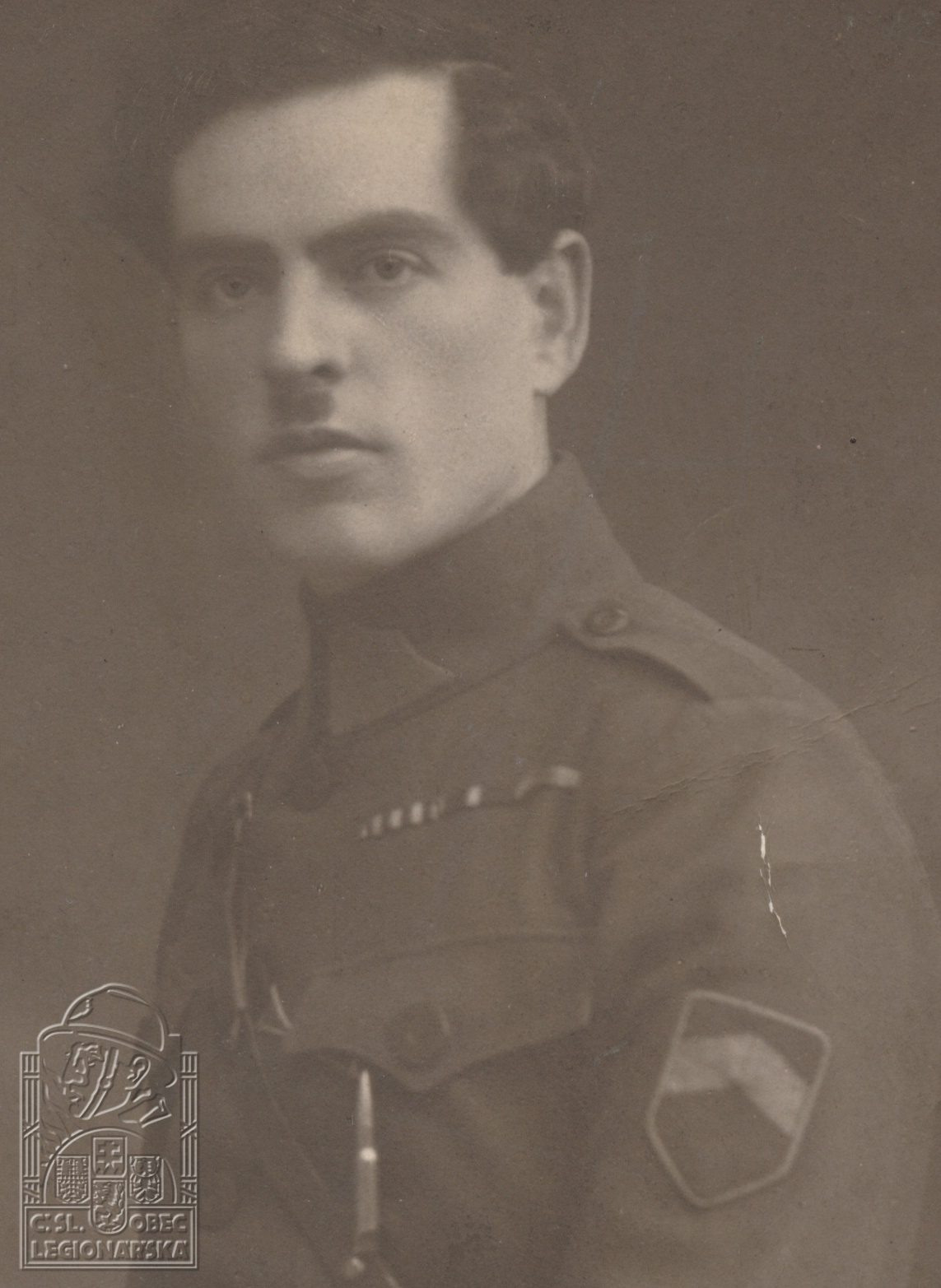A studio portrait of Josef Pěkný in Czechoslovak Legion uniform with a shoulder patch, the emblem of the Czechoslovak Legionary Community embossed in the lower corner