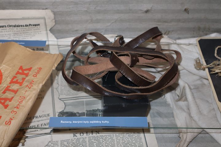 Leather straps laid out on old newspaper beside a museum caption card in Czech, an exhibit at the Police Museum in Prague