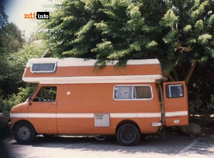An orange and white motorhome parked under a tree, its side door open