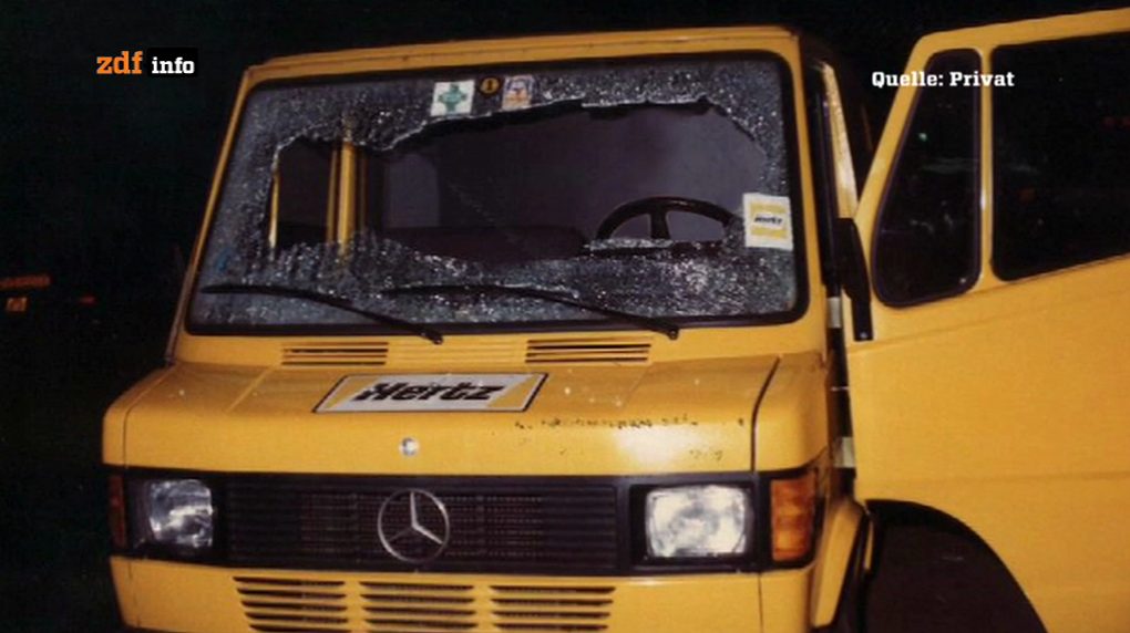 A yellow Hertz van seen from the front, its windscreen shattered, the passenger door open