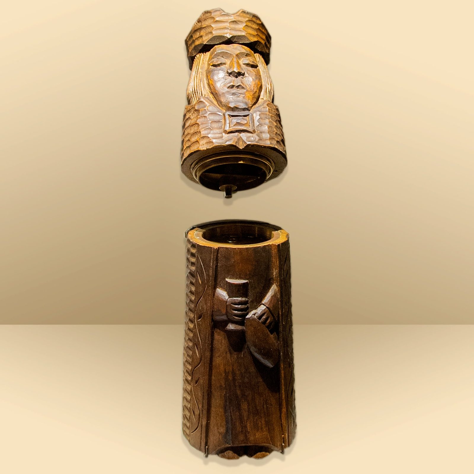 A studio photograph of the same carved wooden figure taken apart in two pieces: the crowned head and shoulders lifted off above the robed body, whose hollow top and brass screw fittings show