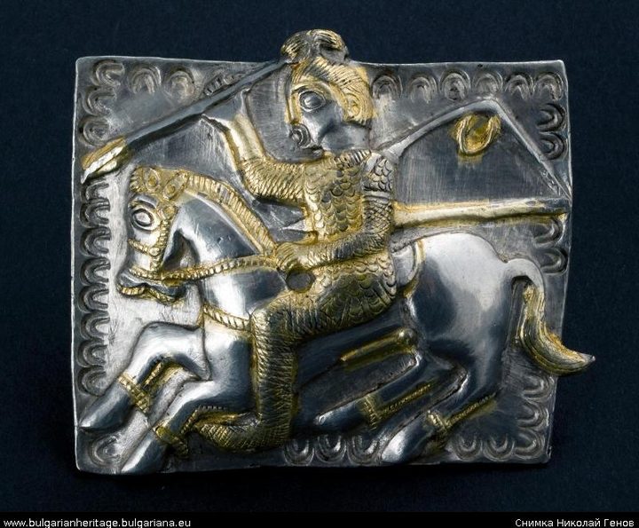A silver harness plate worked in relief and part gilded, showing a rider with a spear on a galloping horse inside a scalloped border